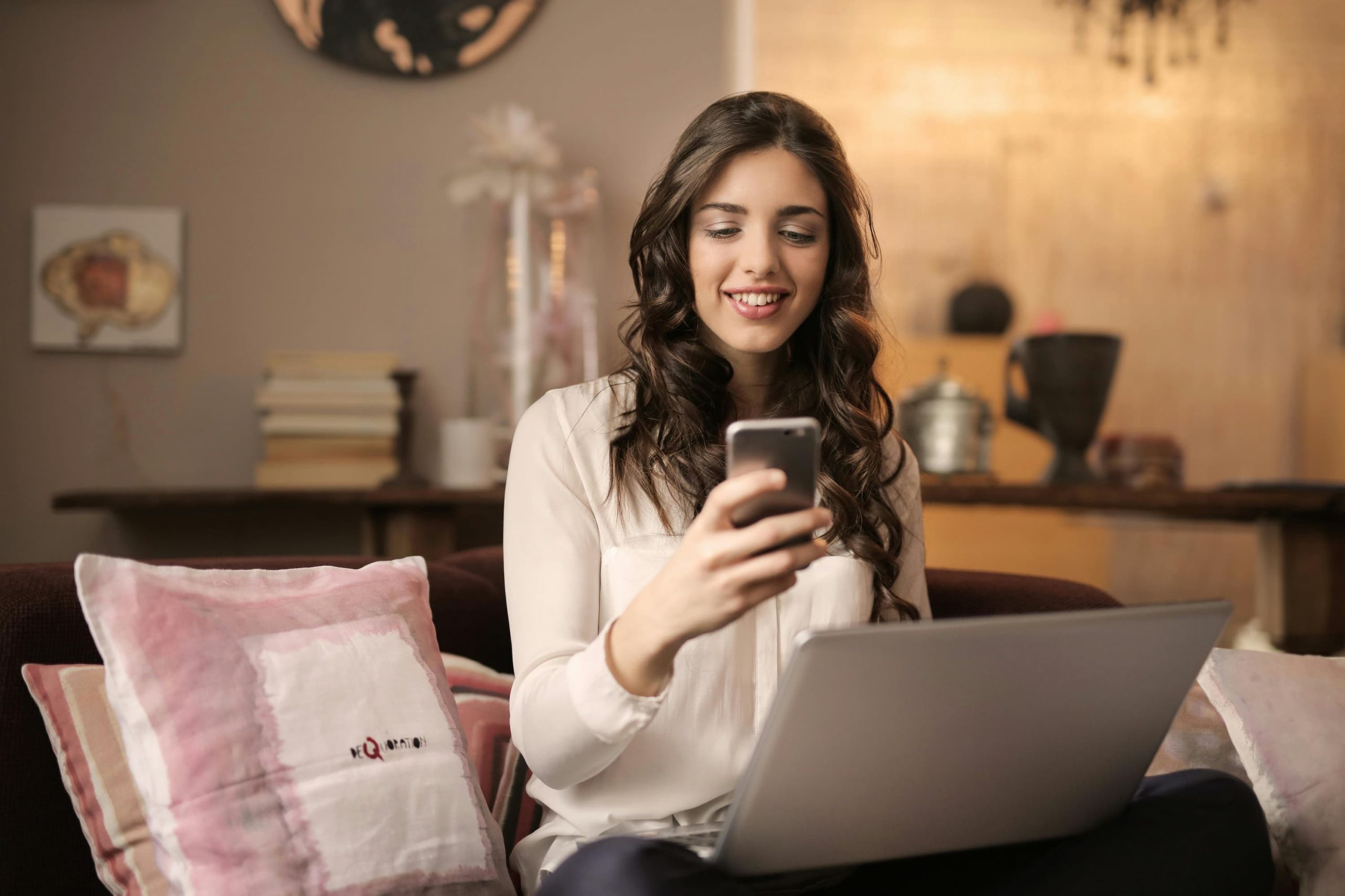 A woman relaxed on a couch with a laptop and cell phone, about to use an exclusive discount for online shopping.