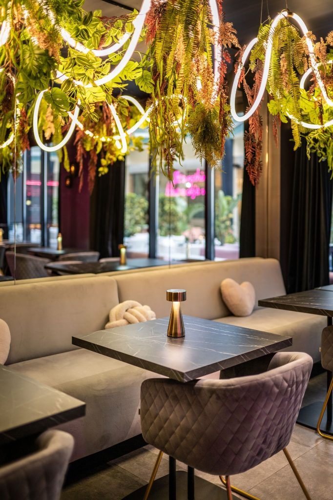 Interior of Baldo Restaurant and Bar featuring tables, chairs, and lush hanging plants for a vibrant dining atmosphere.