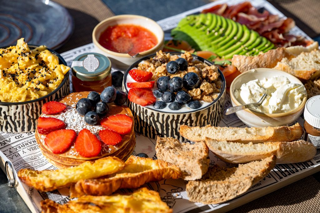 A colorful tray filled with fresh bread, assorted fruits, and various delicious snacks arranged appetizingly.