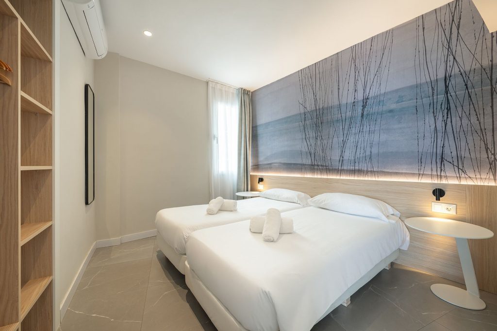 Bright and inviting aparthotel room at Mara boutique, showcasing two beds near each other and an artistic wall mural for a unique touch.