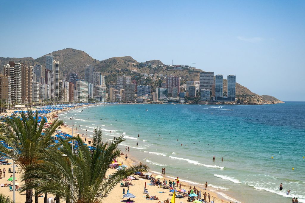 Benidorm beach bustling with visitors enjoying the sun and shade from umbrellas.