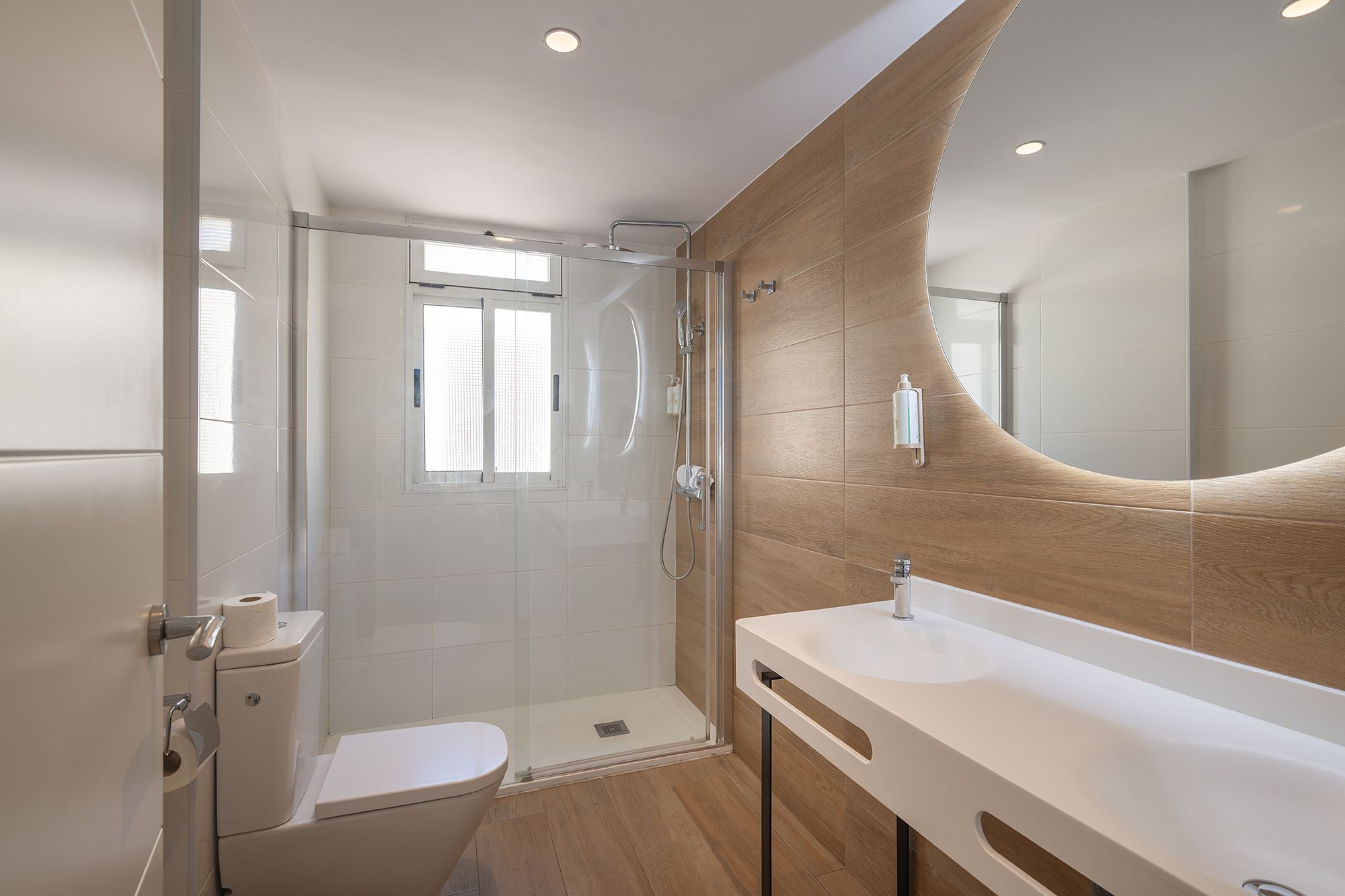 A clean bathroom featuring a toilet, sink, and shower, with neutral-colored tiles and bright lighting.