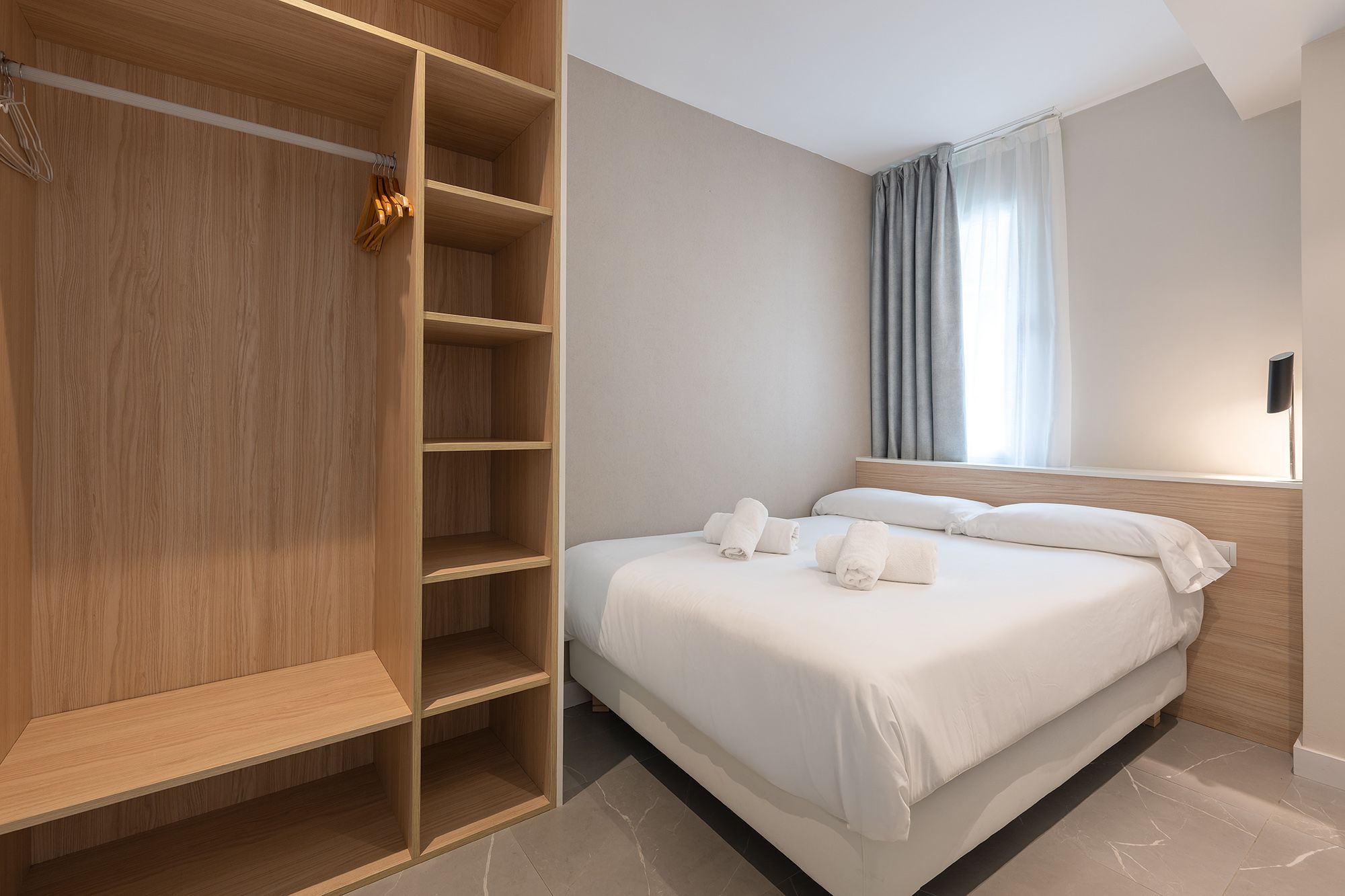 A serene bedroom scene with a comfortable bed, a stylish closet, and wooden shelves adorned with personal items.