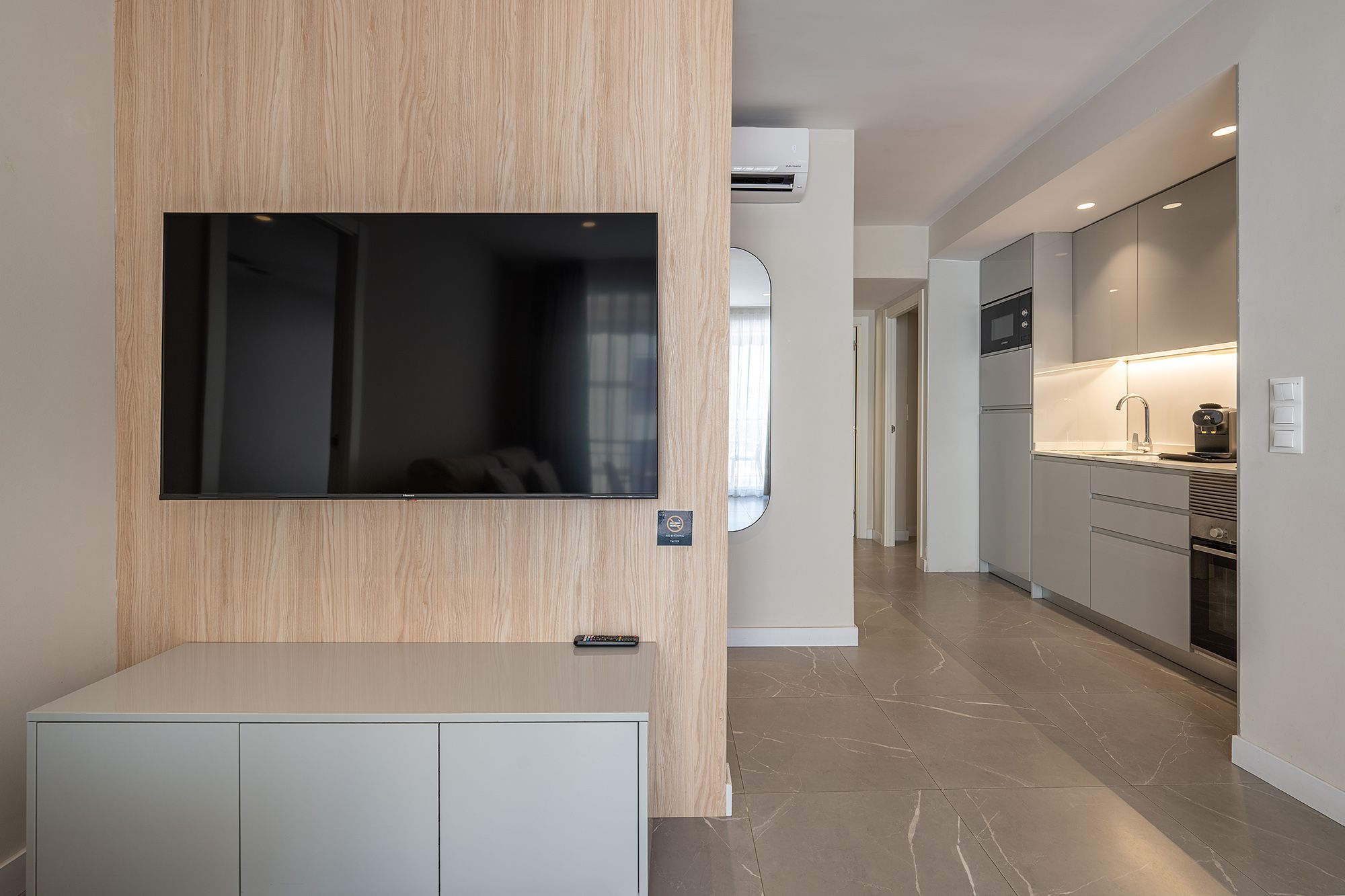 A sleek apartment featuring a wall-mounted TV, an air conditioner, and a section of the kitchen.