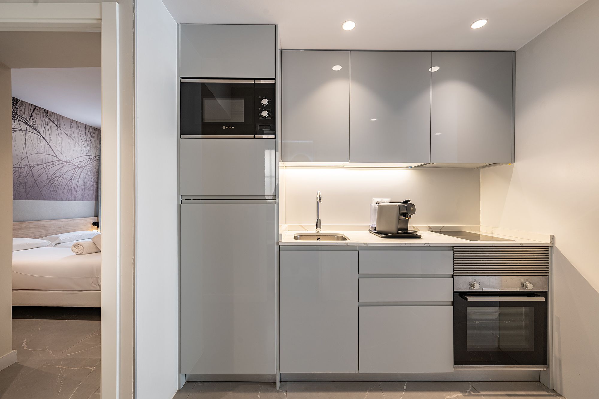 A compact kitchen with essential appliances: a sink, microwave, and oven, coffee machines, designed for efficient cooking.