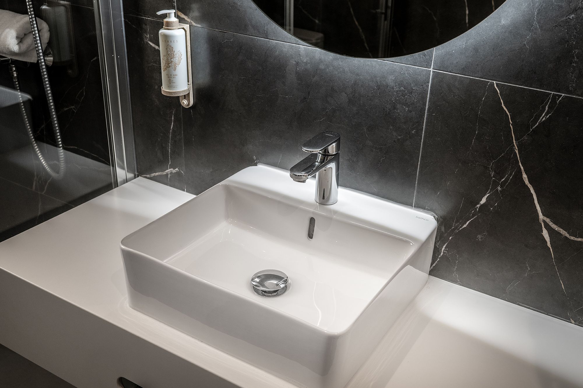 A contemporary bathroom with a circular mirror above the sink, highlighted by a rich black marble wall.