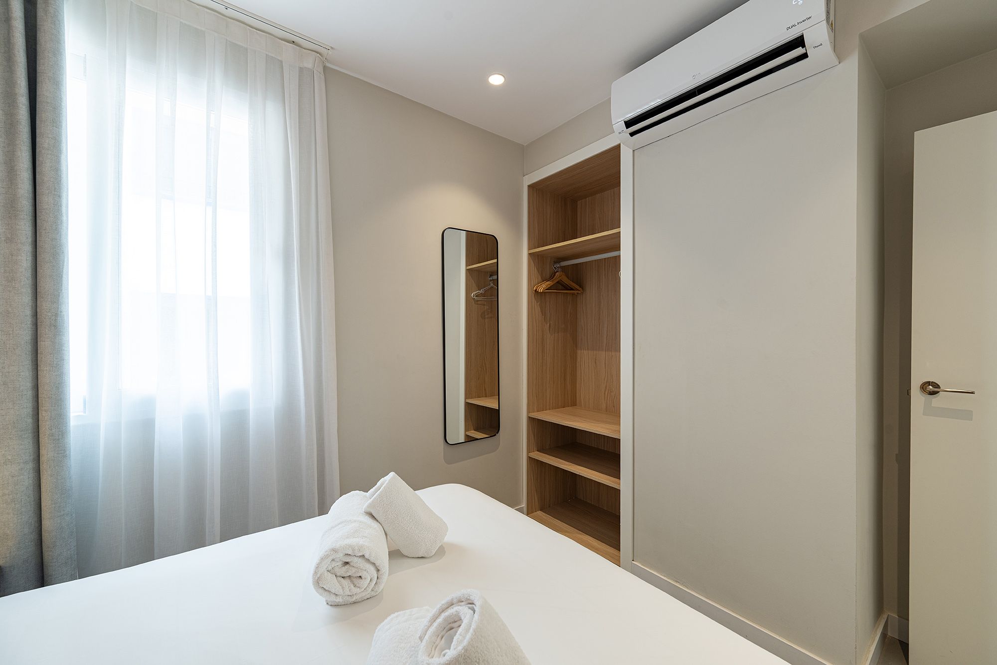 A tidy bedroom featuring a white bed and a spacious closet, creating a serene and organized atmosphere. With air conditioner.