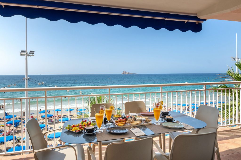 A table set with food and drinks on a balcony, overlooking the ocean from the Mara boutique apartment in Benidorm.