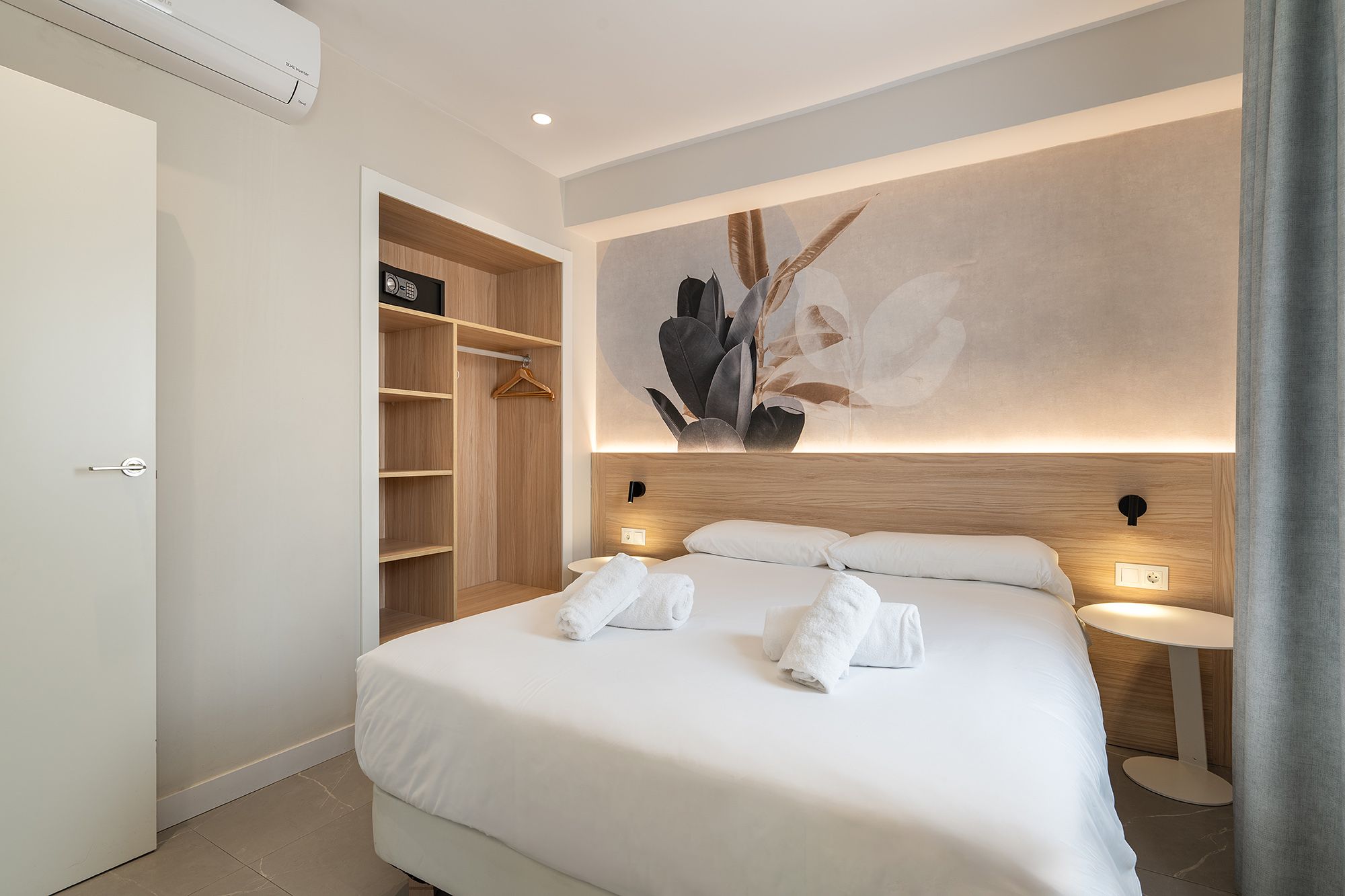 Inviting bedroom with a white bed, decorative wall mural, air conditioning, and free towels, all in a secure environment.