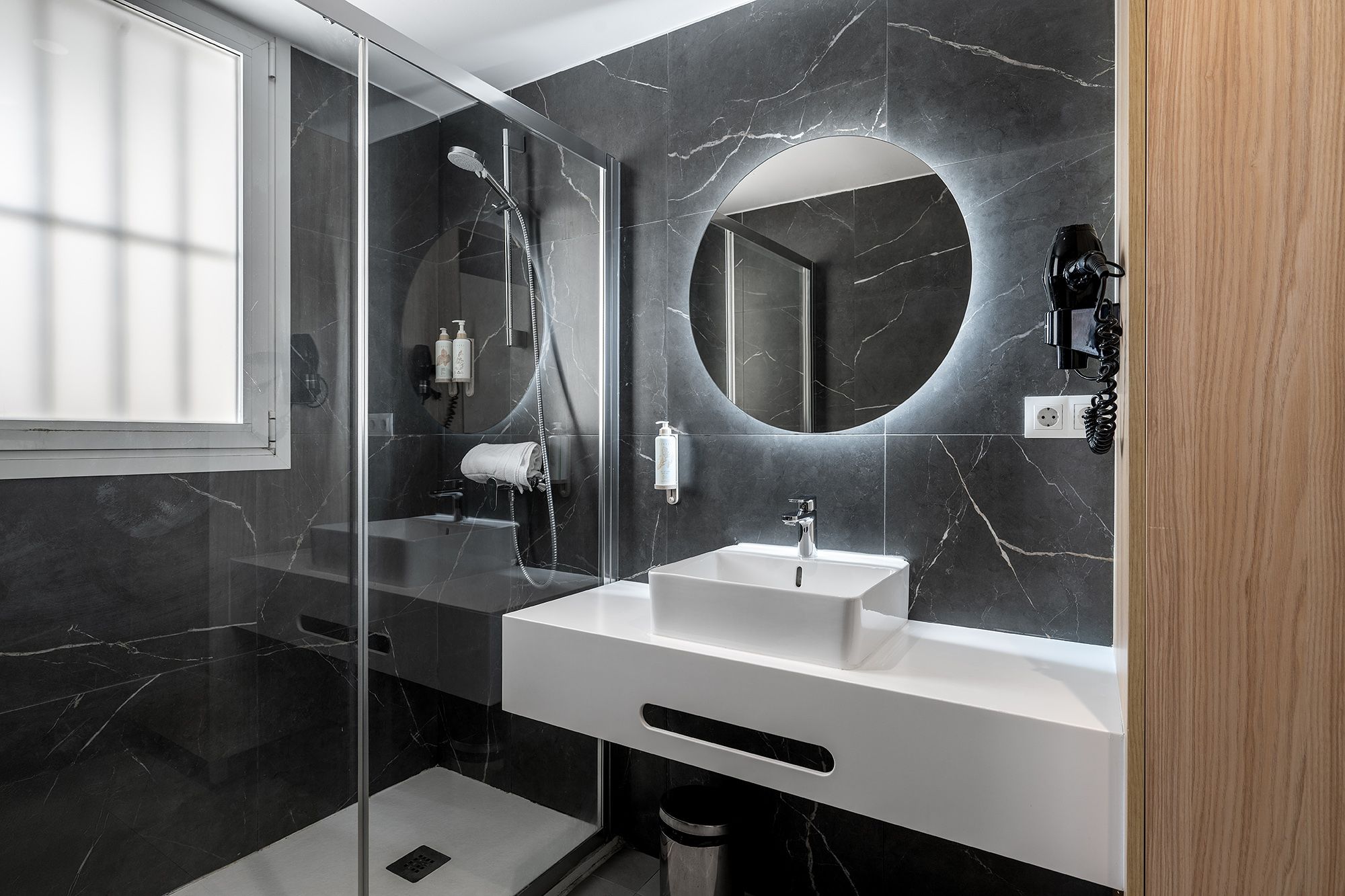 Un baño de diseño chic con un llamativo suelo de mármol negro y una amplia zona de ducha acristalada.