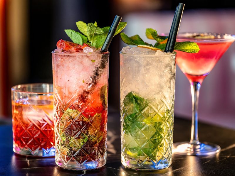 Three colorful cocktails are displayed on a table, showcasing different garnishes and glass styles.