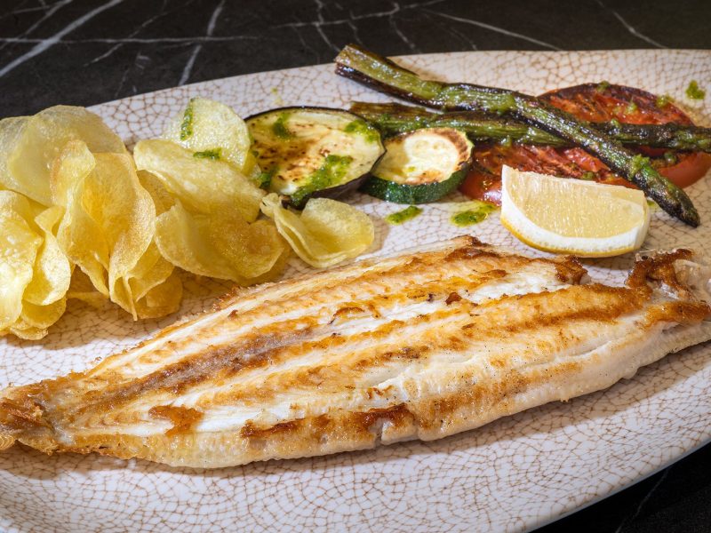 A delicious meal showcasing a perfectly cooked fish, crispy potatoes, and a bright lemon slice on a white plate.