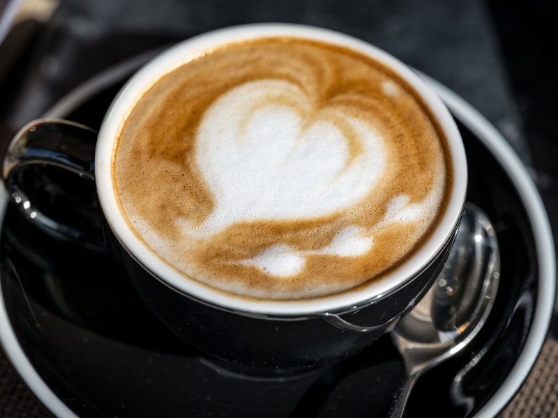 A creamy cappuccino topped with a heart-shaped foam design, served in a white cup on a wooden table.