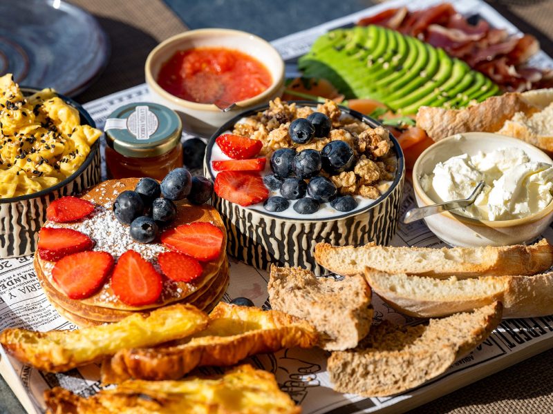 A colorful tray filled with fresh bread, assorted fruits, and various delicious snacks arranged appetizingly.