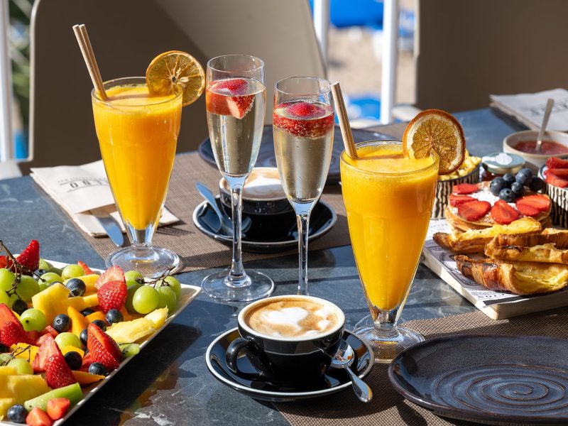 A festive table set with a variety of fruits, a chilled glass of juice, and sparkling champagne for a joyful gathering.