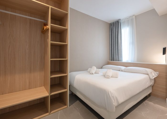 A serene bedroom scene with a comfortable bed, a stylish closet, and wooden shelves adorned with personal items.