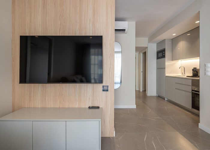A sleek apartment featuring a wall-mounted TV, an air conditioner, and a section of the kitchen.