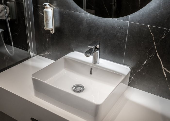 A contemporary bathroom with a circular mirror above the sink, highlighted by a rich black marble wall.