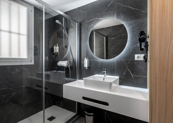 A chic bathroom design with a striking black marble floor and a spacious glass shower area.