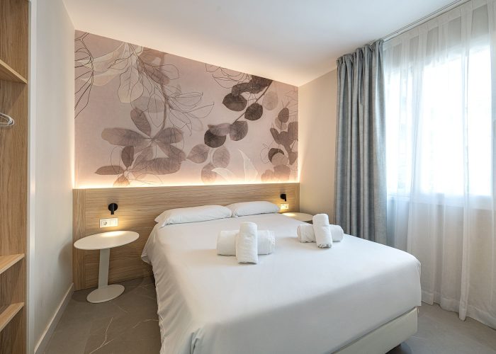 A stylish aparthotel room with a neatly made bed and an artistic wall mural enhancing the ambiance.