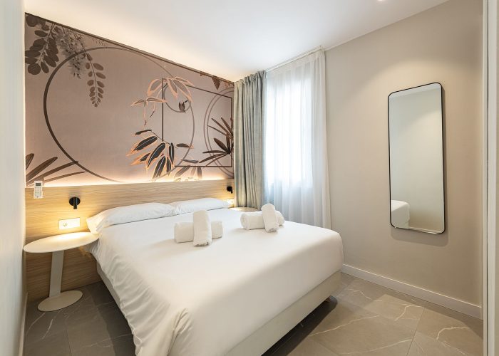 A modern aparthotel room with a soft bed and an eye-catching wall mural, creating a unique and inviting environment.