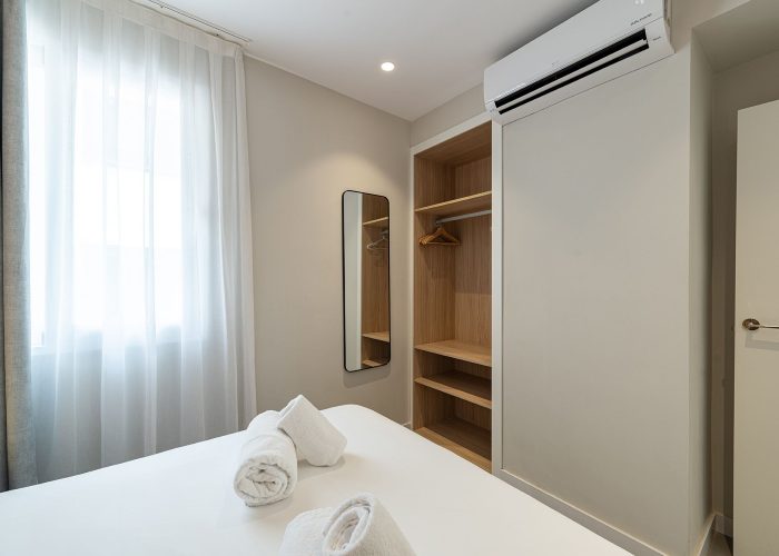 A tidy bedroom featuring a white bed and a spacious closet, creating a serene and organized atmosphere. With air conditioner.